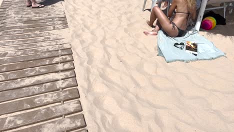 Content-shaped-woman-in-pink-bikini-sitting-on-towel-on-tropical-beach-preparing-the-lunch-in-sunlight