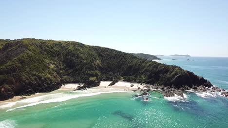 Aerial:-Drone-shot-over-the-ocean-rises-higher-to-reveal-a-stunning-coastal-landscape-that-stretches-up-towards-Byron-Bay-in-New-Wales,-Australia