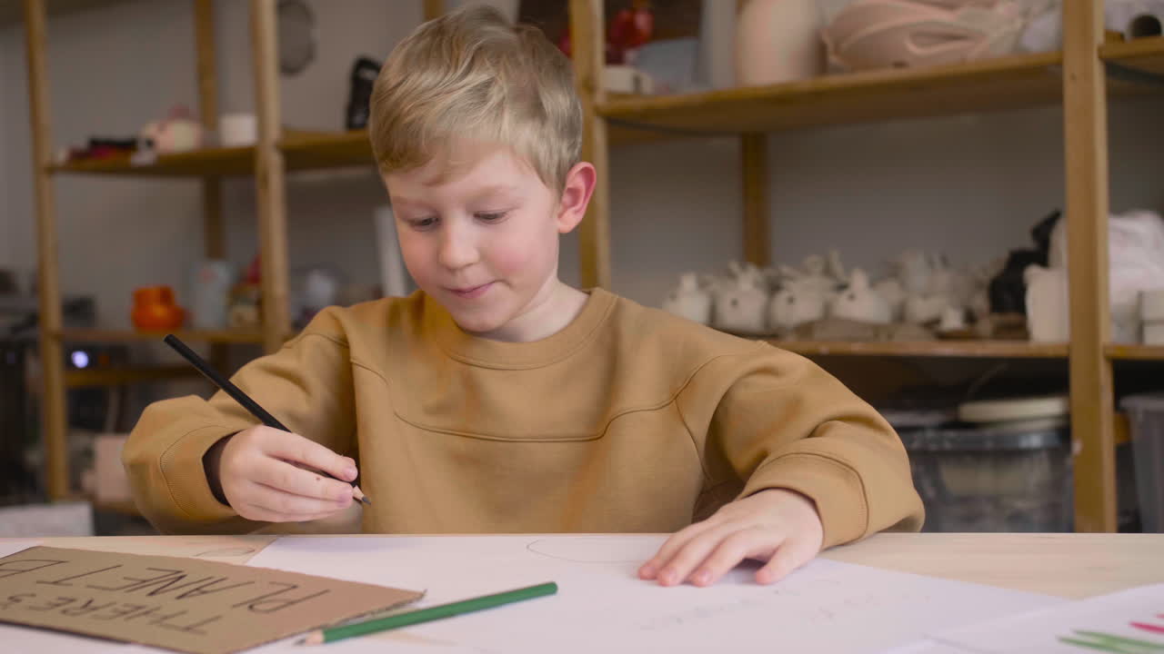 Blond kid drawing sitting at a table in a craft workshop
