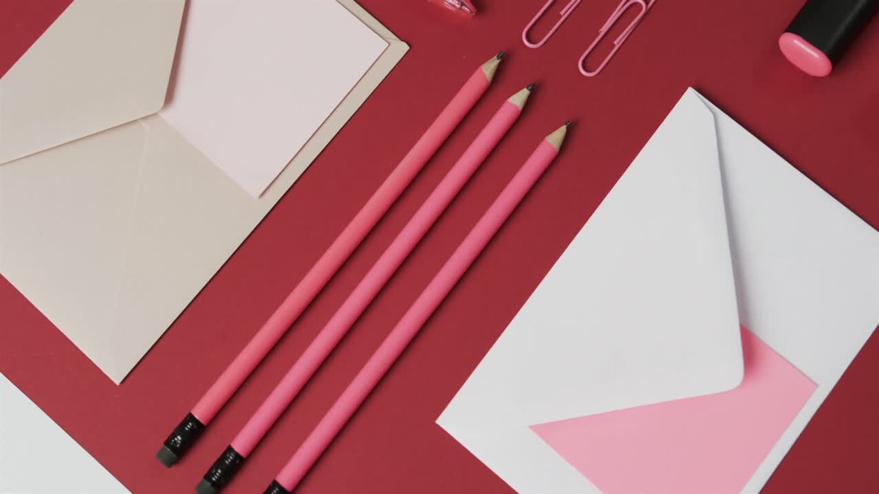vista aérea de bolígrafos, lápices y papelería dispuestos sobre un fondo rojo, en cámara lenta