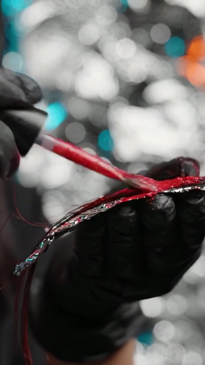 Applicazione di una vivace tintura rossa su ciocche di capelli usando un pennello su carta stagnola per una trasformazione dei capelli sorprendente e audace in un'atmosfera creativa e artistica.