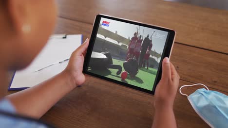 composite of woman sitting at table with face mask, watching hockey match on tablet