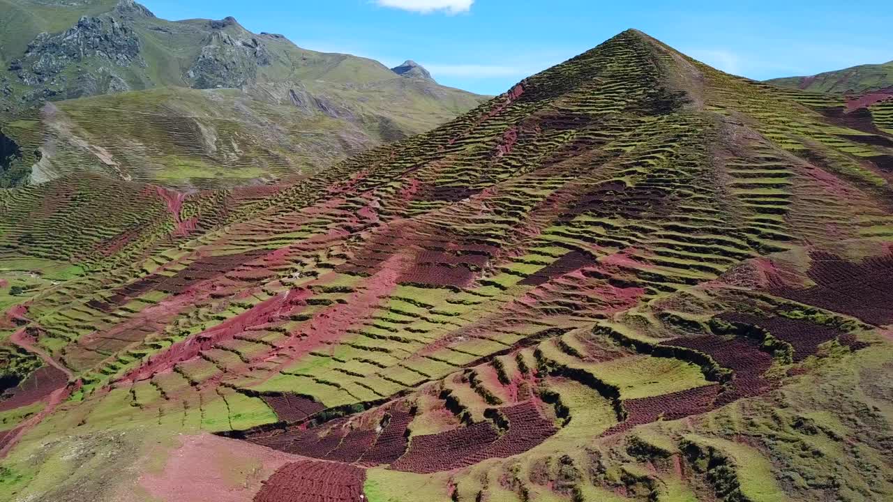 Aerial, tracking, drone shot overlooking green and red terraces and mountains, on a sunny day, in Cusco, Peru, South America