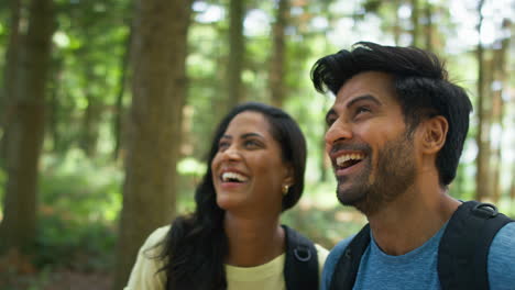 Couple-With-Backpacks-Hiking-Or-Walking-Through-Woodland-Countryside-In-Summer-Enjoying-Nature