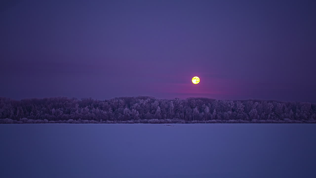 보름달은 대기 구름 아래에서 눈밭 너머 숲으로 내려갑니다 - 야간 시간 경과