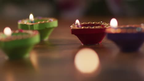 four lit candles in decorative clay pots on wooden table top, bokeh flame in foreground