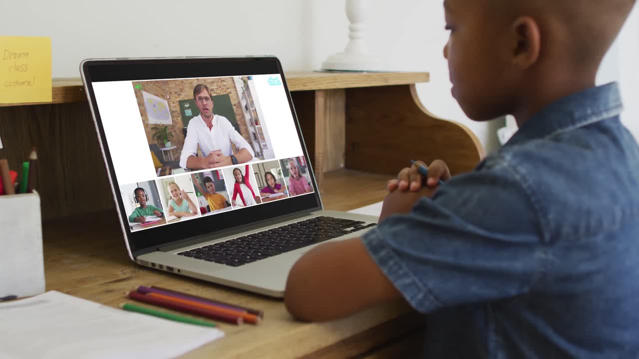 Schoolboy using laptop for online lesson at home, with diverse teacher and class on screen