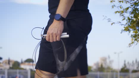 Tracking-shot-of-an-athletic-man-holding-skipping-ropes-and-walking