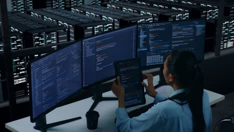 side view of asian woman developer working with tablet while write code with multiple computer screens in data center