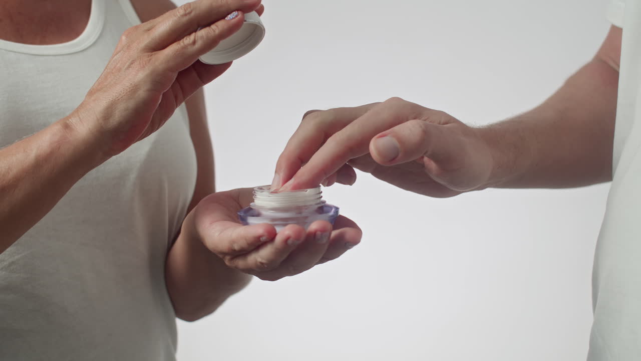 Hands Taking Cream from Jar Held by Another Person