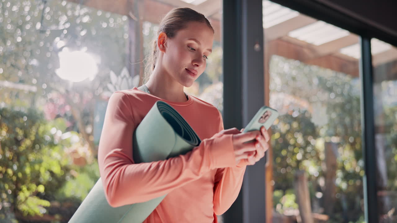 mujer comprobando su teléfono mientras sostiene su colchón de yoga