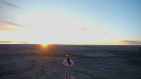 puesta de sol sobre el paisaje gris del desierto y una chica solitaria de pie en un acantilado con una vista impresionante