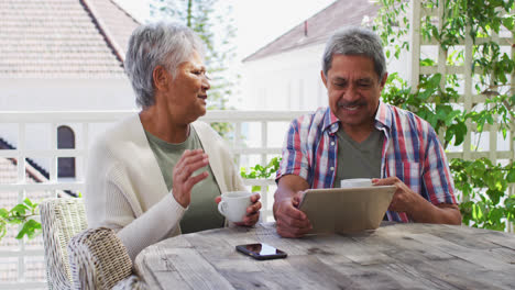 Älteres-Gemischtrassiges-Paar-Beim-Kaffeetrinken-Mit-Tablet-Im-Garten