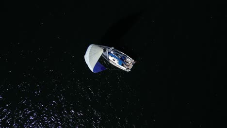 Top-down-view-of-a-sailboat-sailing-on-the-dark-water-of-the-baltic-sea,-static-drone-shot,-high-contrast-scene