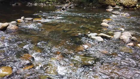 Crystal-clear-white-water-flowing-downstream-over-stones-and-pebbles-which-make-up-the-riverbed