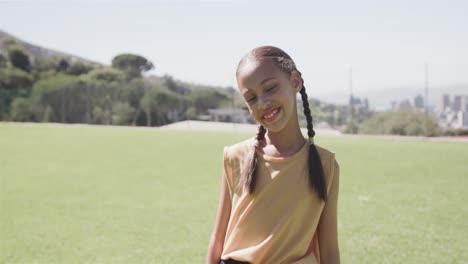 Portrait-of-happy-biracial-girl-on-sunny-elementary-school-playing-field,-slow-motion