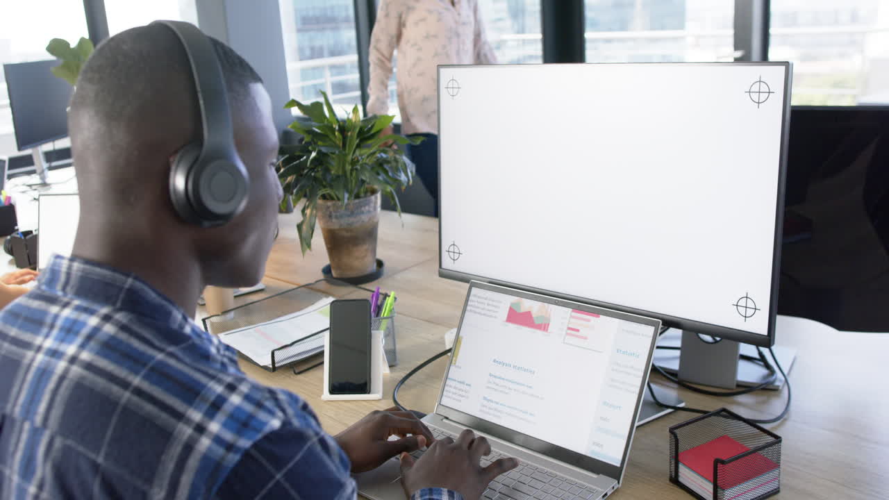 African american businessman using computer with blank screen in office, slow motion, copy space