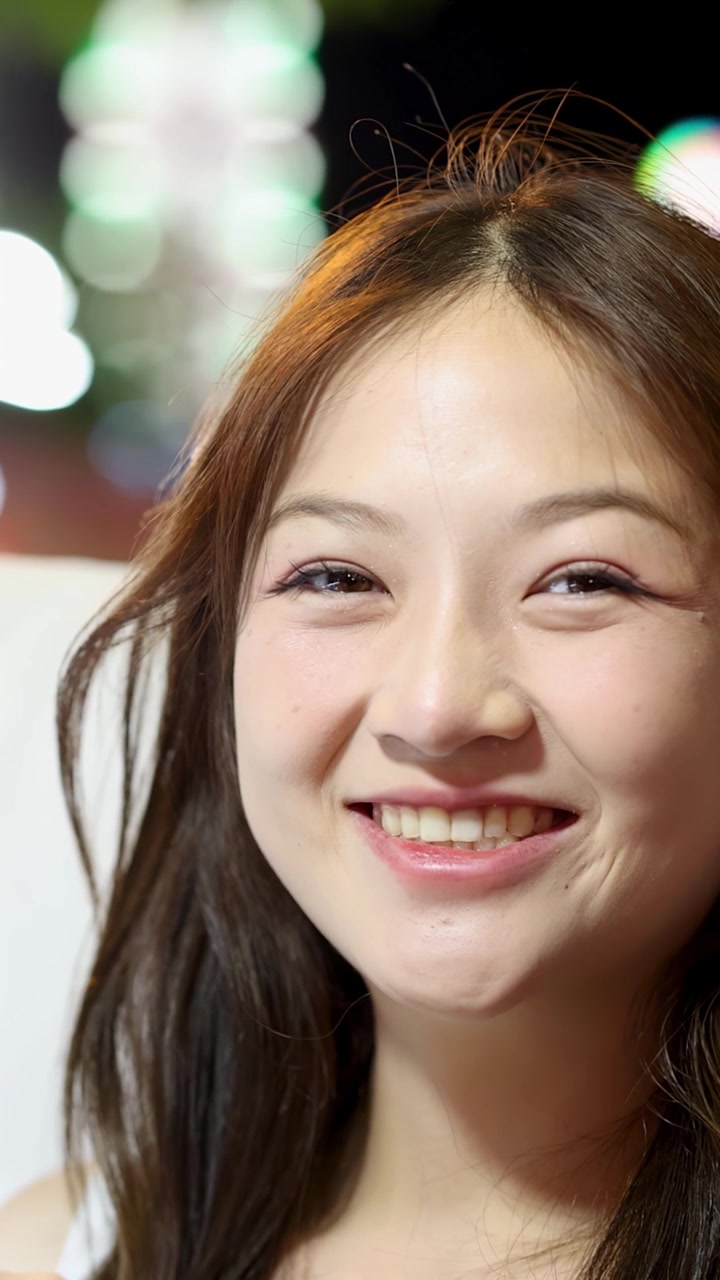 明るいナイトマーケットの光の下で、飴がけフルーツの串を持つ陽気な若い女性のクローズアップ。