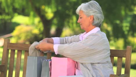 mujer madura en un banco del parque con sus compras