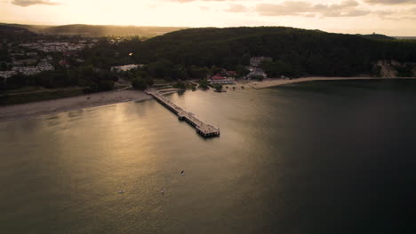 4k aerial view of the sunset at a pier in the sea with a mountain with woods