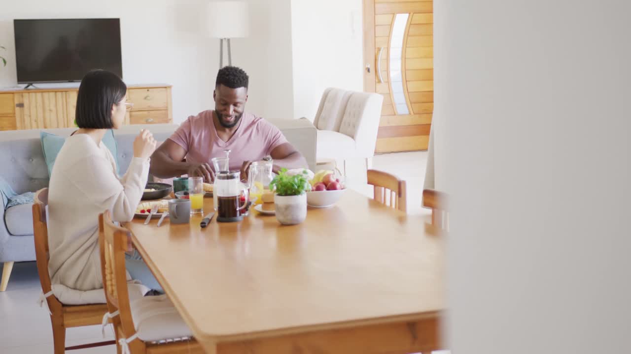 pareja feliz y diversa sentada a la mesa y desayunando