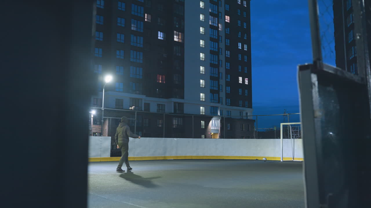 el atleta patea una pelota de fútbol hacia la meta bajo las luces brillantes del estadio en el campo deportivo urbano, enmarcado por altos edificios residenciales y un cielo nocturno azul vívido