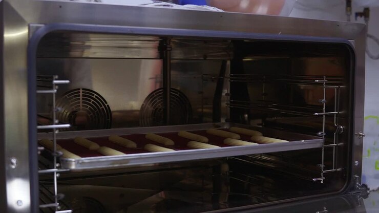 Putting a baking tray with eclaires or profiteroles on it into the oven. Confectioners work.