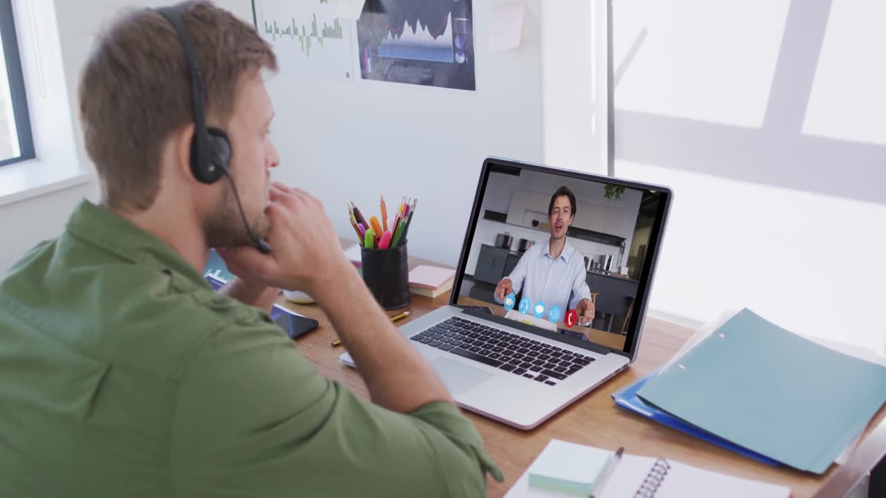 Kaukasisk mand bruger bærbar computer og telefonheadset på videoopkald med en mandlig kollega.