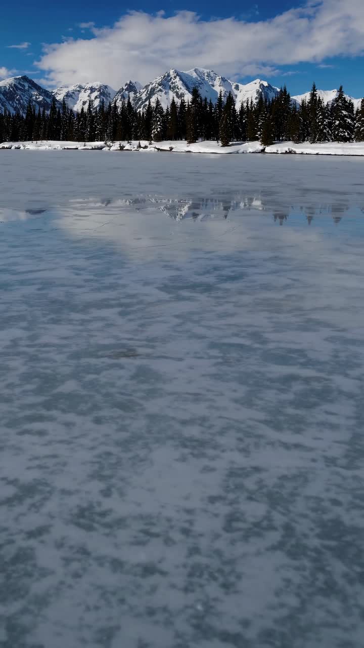 A stunning wide-angle view of a frozen lake with snow-capped mountains and pine trees, perfect