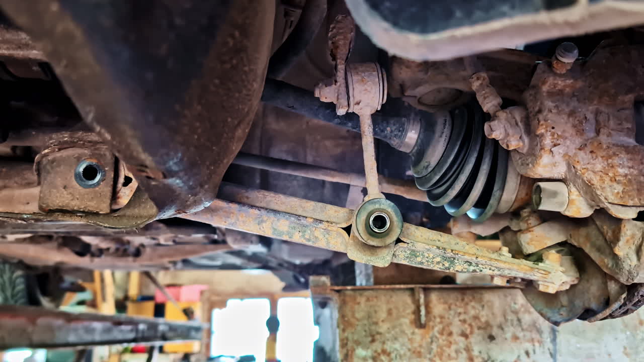 Front control arm removed from vehicle exposing rusted suspension and axle components