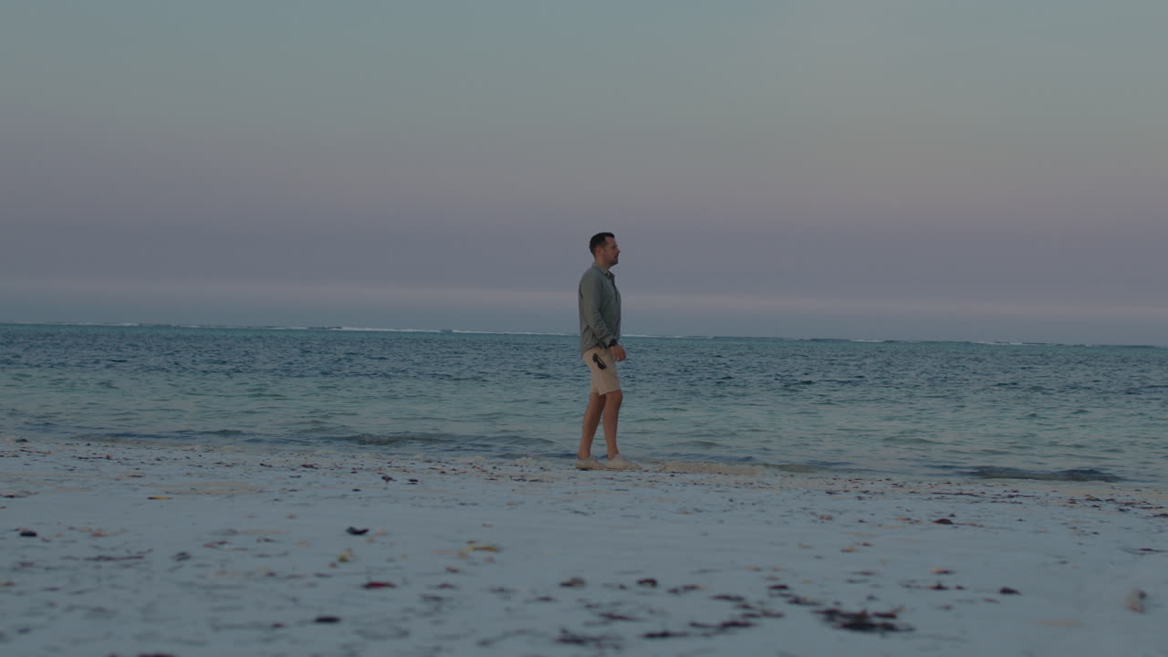 Man Walking on a Peaceful Beach at Sunset
