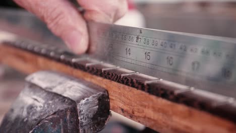 a luthier measuring the distance between frets of a guitar with a metal measuring stick - close up