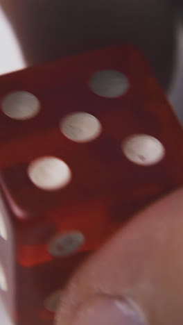 man turns red plastic dice with symbols five of spots on sides against white surface extreme close view