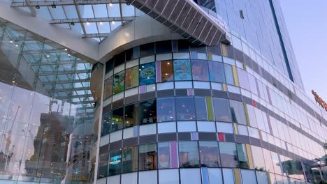 camera tilts upward along a contemporary glass and steel shopping mall facade in singapore, capturing architectural details in bright daylight with clear skies