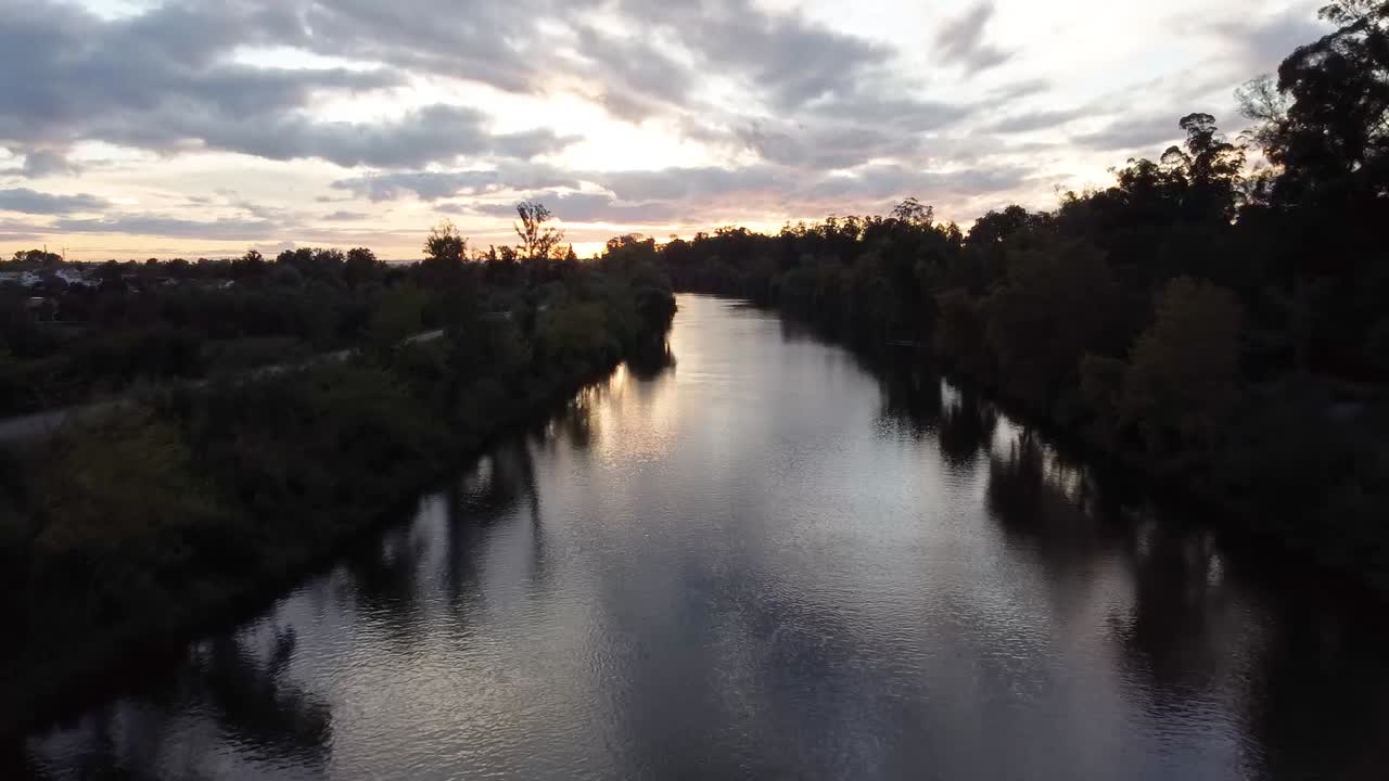 drone volando sobre el río durante la puesta de sol cerca de un bosque