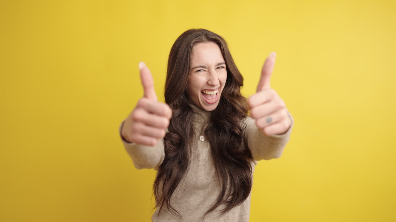 Enthusiastic young woman showing thumbs up on yellow background