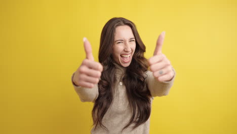 enthusiastic young woman showing thumbs up on yellow background