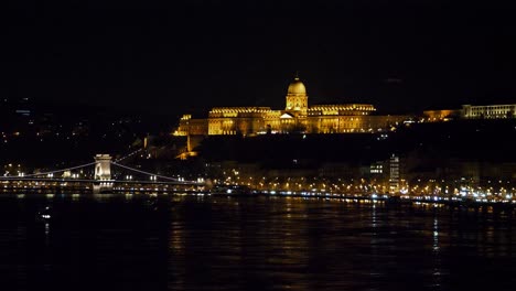 Vista-Del-Centro-De-La-Ciudad-De-Budapest-Con-El-Castillo-De-Buda-Y-El-Río-Danubio-Por-La-Noche,-Arquitectura-Gótica,-Reflejos-De-Luz,-Amplia-Toma-Panorámica