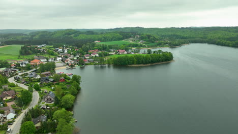 Vista-Aérea-Del-Pueblo-De-Ostrzyce-Junto-A-Un-Lago,-Rodeado-De-Exuberantes-Colinas-Y-Bosques-Verdes