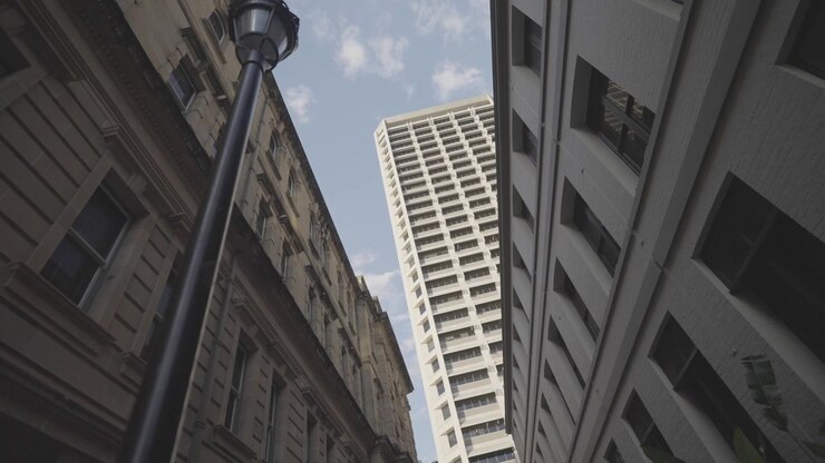 Una vista dal basso tra un edificio storico in arenaria e una moderna torre cittadina, con un lampione nell'inquadratura