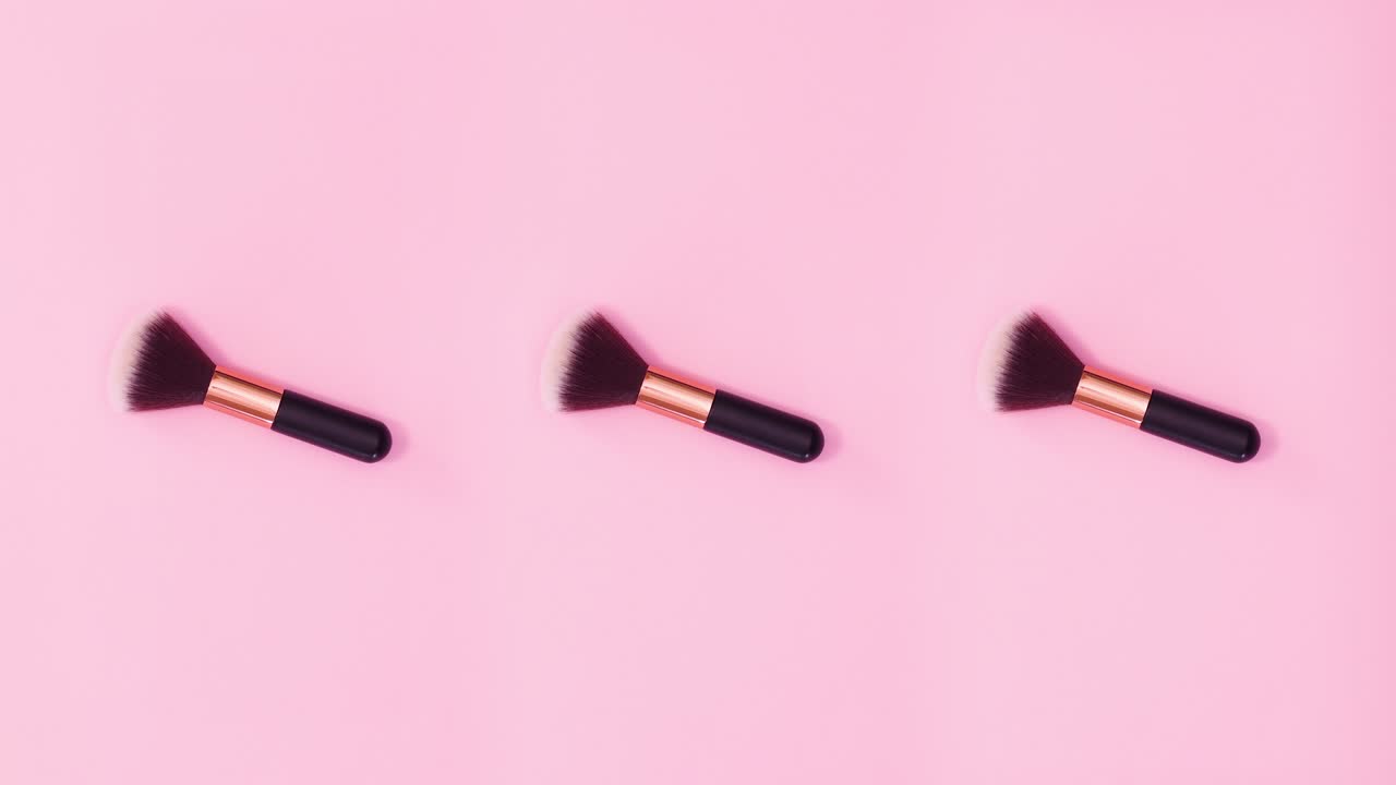Tre makeupbørster roterer på en lyserød baggrund. Stop-motion.