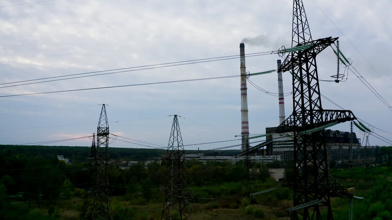 Electricity towers on factory background. High-voltage electric pylons near the harmful enterprise. The concept of nature and technology. Camera rising up.