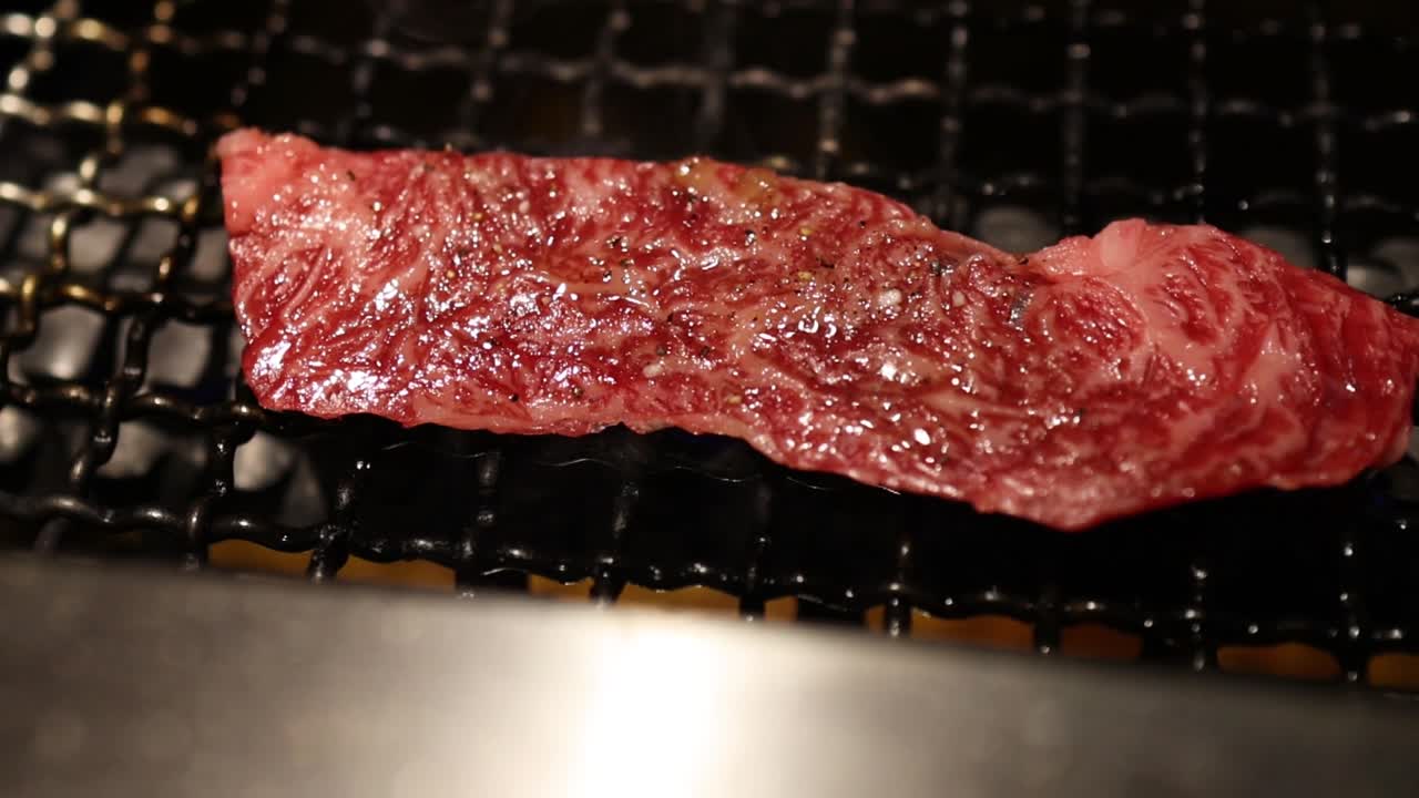 Close-up of marbled beef strips being grilled over an open flame on a metal grate.