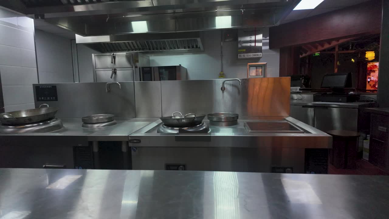 Zeitlupe einer Nahaufnahme von leeren Edelstahl-Woks auf leistungsstarken Brennern in einer professionellen Shanghaier Restaurantküche, sauber und bereit