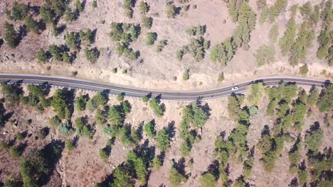quedarse quieto toma aérea de un automóvil que sube la colina en una sinuosa carretera del medio oeste en las montañas con pinos