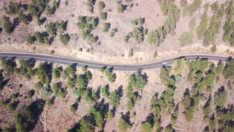 stand still aerial shot of a car driving up the hill on a winding mid-western road in the mountains with pine trees