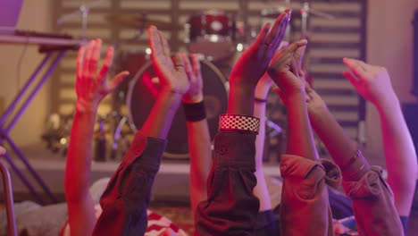 Close-Up-Of-Unrecognizable-Multiethnic-Friends-Moving-Their-Raised-Hands-In-The-Air-While-Lying-On-The-Floor-During-Rehearsal-In-Recording-Studio