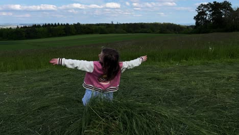 una niña pequeña jugando y cae de espaldas sobre un montón de hierba cortada en un campo