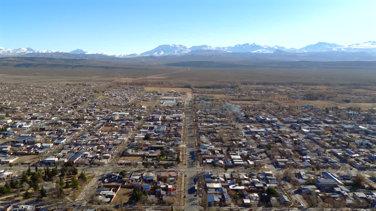 low descending aerial of Malargüe in southern Mendoza with clear view of the Andes mountain range and structured urban grid amid arid landscape and sharp geographic contrast in the background