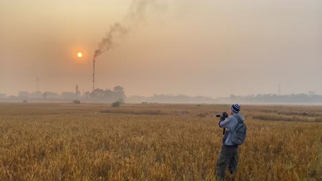 Photojournalist-taking-photos-of-industry-area-in-Bangladesh,-standing-on-field